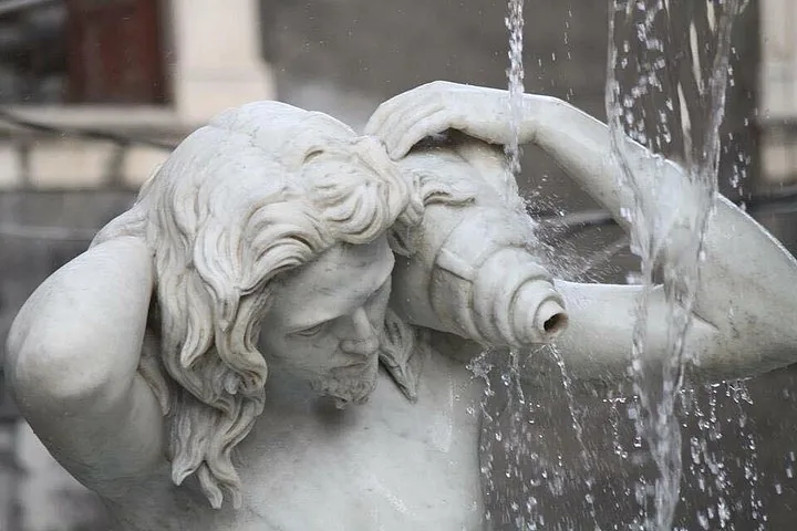 Nahaufnahme einer weißen Marmorbrunnenstatue eines Mannes, der eine Muschel hält.
