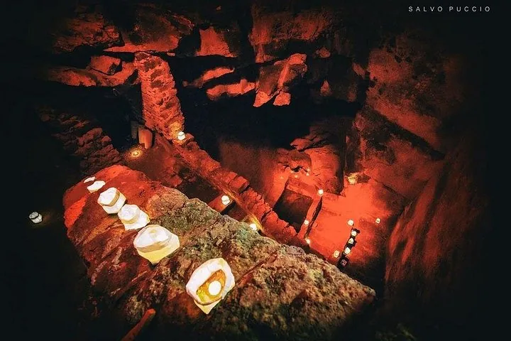 Eine unterirdische Steinanlage, beleuchtet von zahlreichen kleinen Kerzen, die ein rotes Leuchten erzeugen.