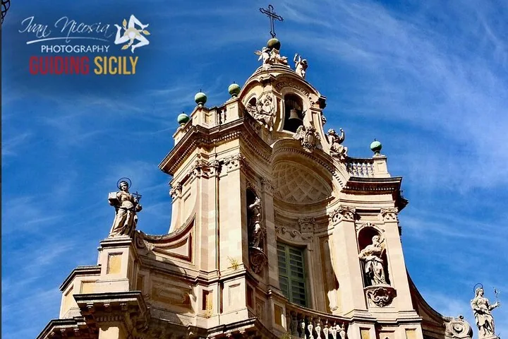 Die verzierte obere Fassade und der Glockenturm der Kathedrale von Catania vor blauem Himmel.