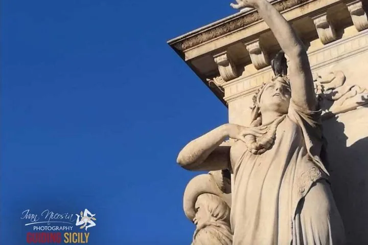 Eine Steinstatue einer Frau mit erhobenem Arm und einem Vogel auf dem Kopf.