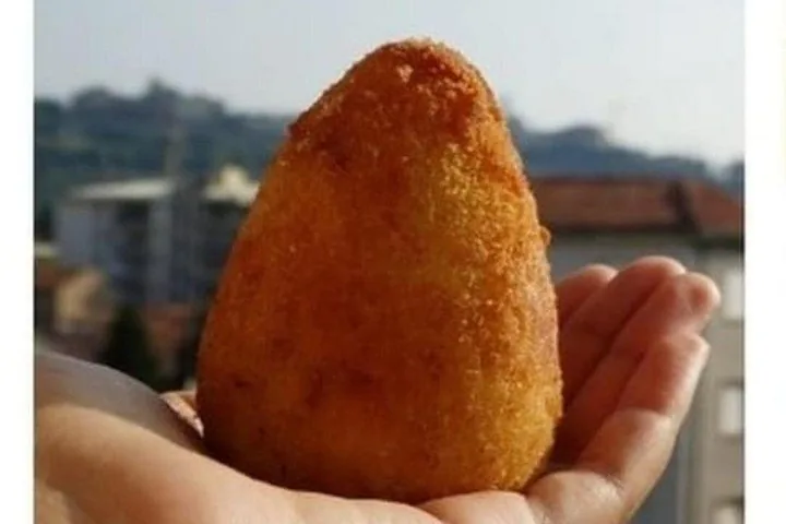 Eine Hand hält einen großen, goldenen, kegelförmigen frittierten Arancino.